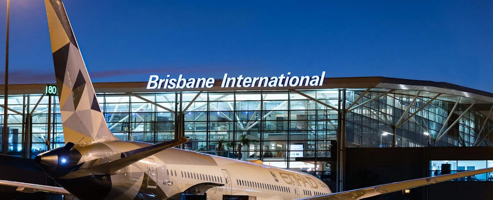 Brisbane International Airport terminal at dusk with an aircraft parked at the gate.