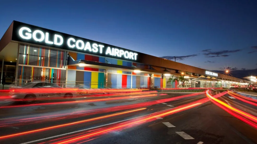 The colourful Gold Coast Airport terminal at night with car light trails streaking past.